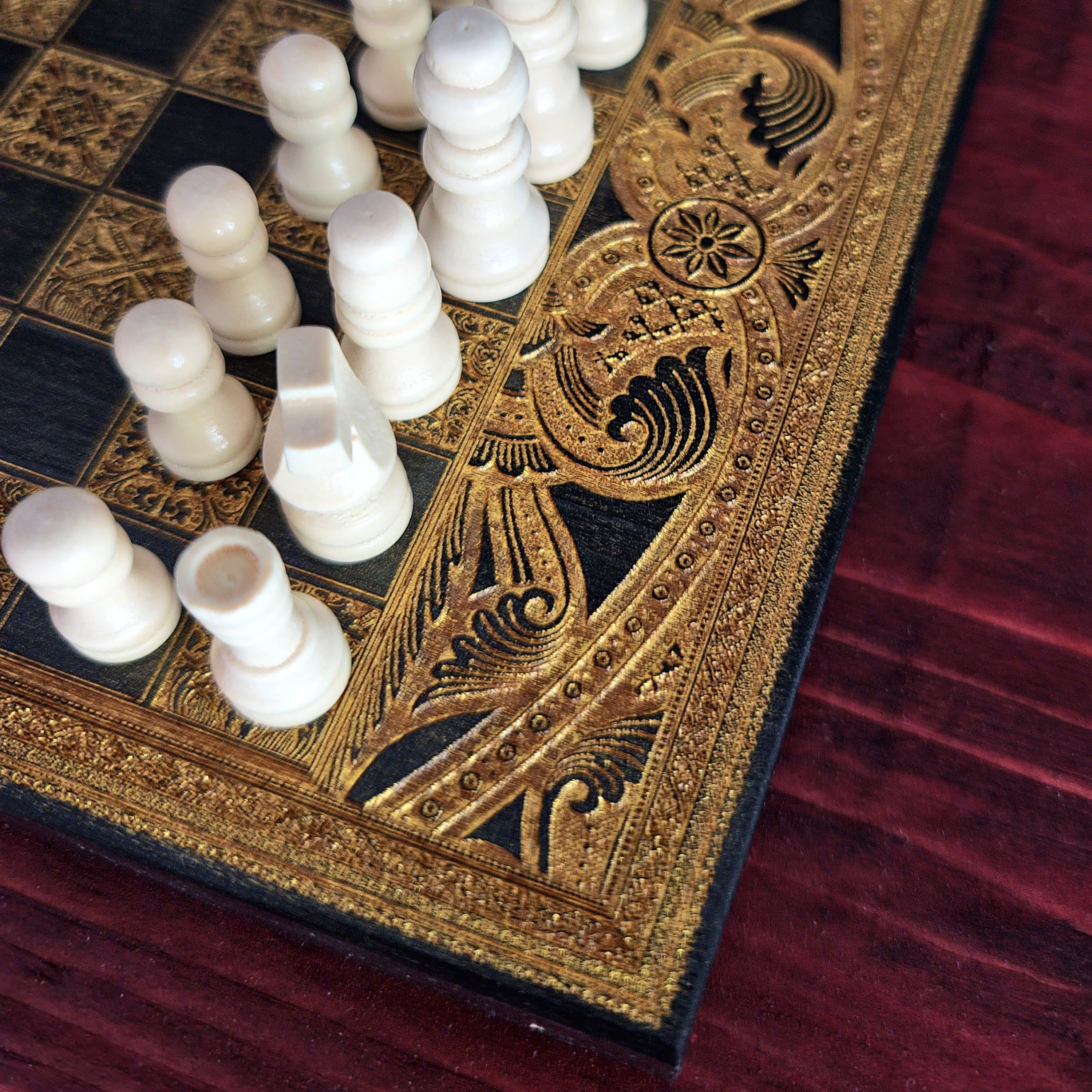 An ornate chess set with carved ivory chess pieces and a black board featuring intricate gold filigree borders, set 