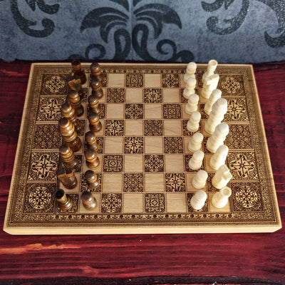 An ornate wooden chessboard with engraved patterns, set with dark brown and off-white chess pieces