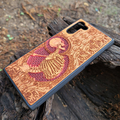 Close-up of handcrafted cherry wood phone case featuring intricate laser-engraved Gothic skeleton artwork.