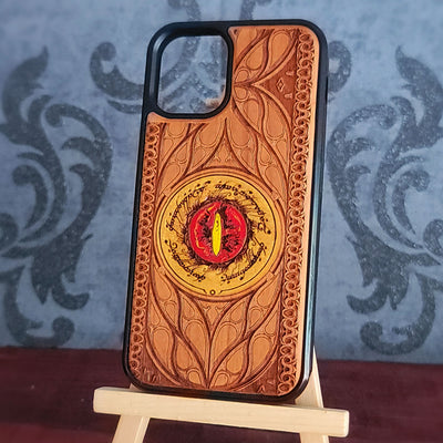 A phone case with an embossed Hobbit door design featuring a red and yellow eye of Sauron in the center, displayed on a small wooden stand.