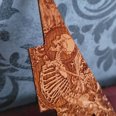 Close up of human skeleton artwork engraved into natural cherry wood guitar pickguard
