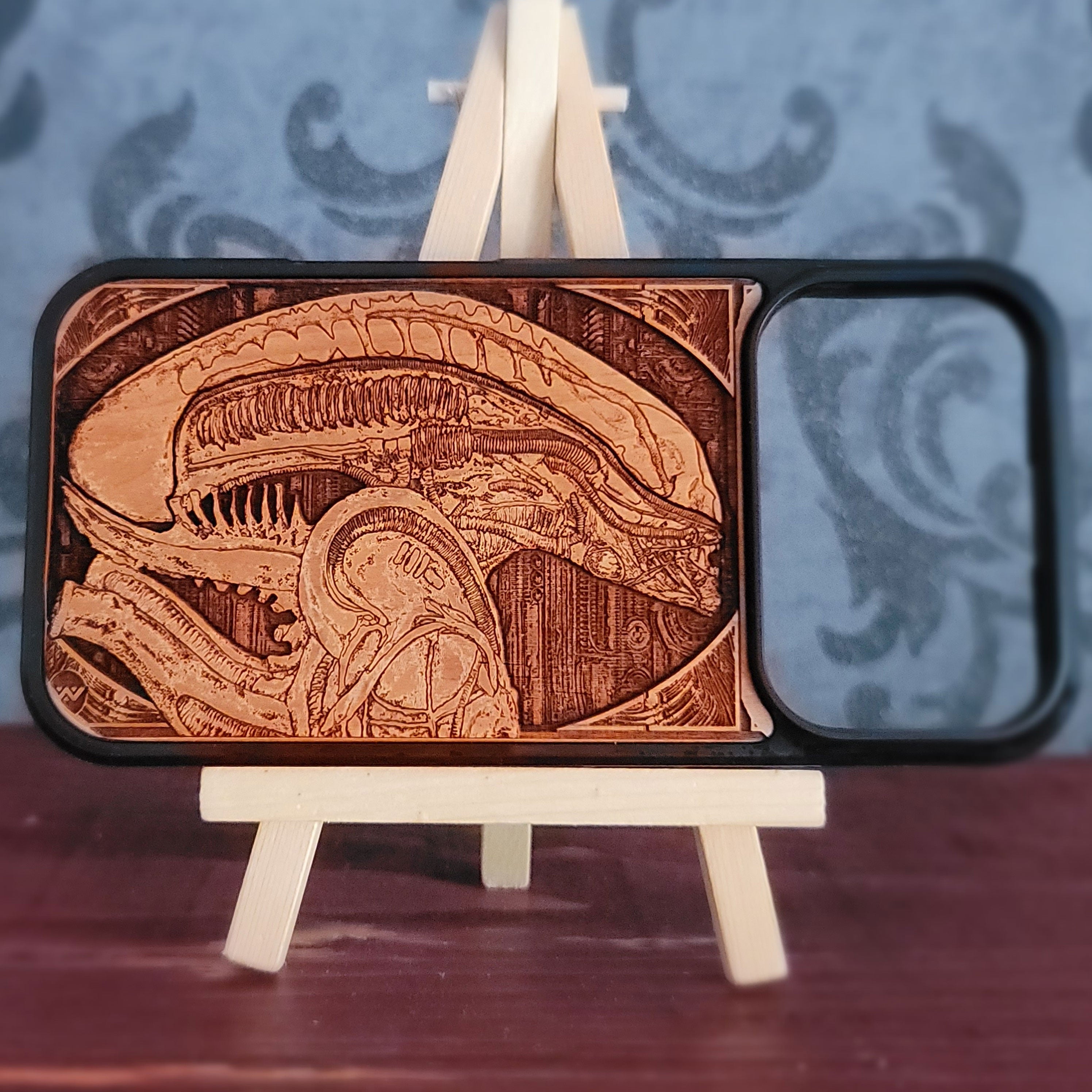 A wooden phone case with a detailed laser-engraved Alien Xenomorph design