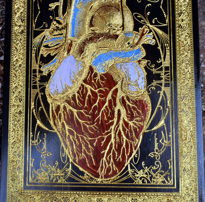 Engraved anatomical heart design painted black and gold on wood panel.