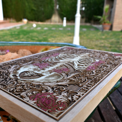 Buried skeleton wood art featuring red flowers, gothic horror-style decor.