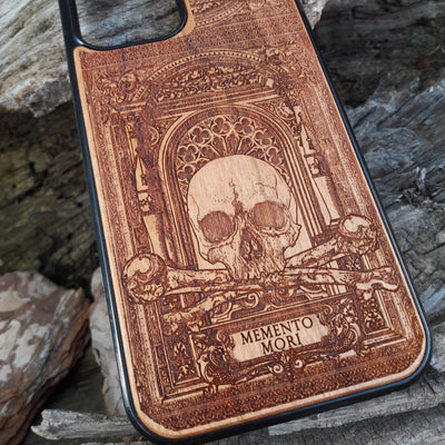 Laser-engraved Memento Mori wood phone case featuring a skull, crossbones, and intricate Gothic patterns with "Memento Mori" text for iPhone  and Samsung Galaxy S. Perfect for Gothic and philosophical design lovers.