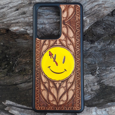 Wooden phone case for iPhone and Samsung Galaxy featuring the 'Smiley' symbol from the Watchmen saga, laser-engraved for a unique touch. Compatible with iPhone 15, 14, 13, 12, 11 Pro Max Mini and Samsung Galaxy S24, S23, S22, S21, S20 Ultra Plus Note 20. Slim, durable, and stylish—order now to make a statement!