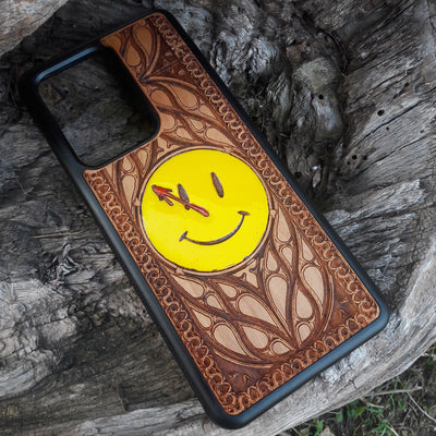 Wooden phone case for iPhone and Samsung Galaxy featuring the 'Smiley' symbol from the Watchmen saga, laser-engraved for a unique touch. Compatible with iPhone 15, 14, 13, 12, 11 Pro Max Mini and Samsung Galaxy S24, S23, S22, S21, S20 Ultra Plus Note 20. Slim, durable, and stylish—order now to make a statement!