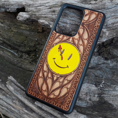 Wooden phone case for iPhone and Samsung Galaxy featuring the 'Smiley' symbol from the Watchmen saga, laser-engraved for a unique touch. Compatible with iPhone 15, 14, 13, 12, 11 Pro Max Mini and Samsung Galaxy S24, S23, S22, S21, S20 Ultra Plus Note 20. Slim, durable, and stylish—order now to make a statement!