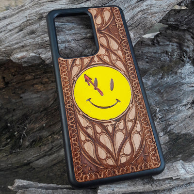 Wooden phone case for iPhone and Samsung Galaxy featuring the 'Smiley' symbol from the Watchmen saga, laser-engraved for a unique touch. Compatible with iPhone 15, 14, 13, 12, 11 Pro Max Mini and Samsung Galaxy S24, S23, S22, S21, S20 Ultra Plus Note 20. Slim, durable, and stylish—order now to make a statement!